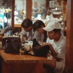 Suasana meja panjang di kedai kopi dengan orang-orang berbincang di malam hari.