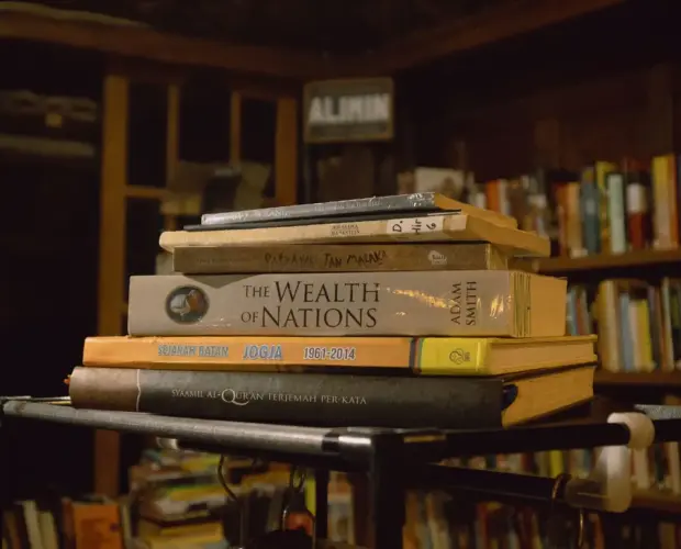 Tumpukan koleksi buku baru termasuk The Wealth of Nations dan Al-Quran di rak besi Pustaka TB Alimin, fasilitas kedai kopi dengan taman baca di Dongeng Kopi.